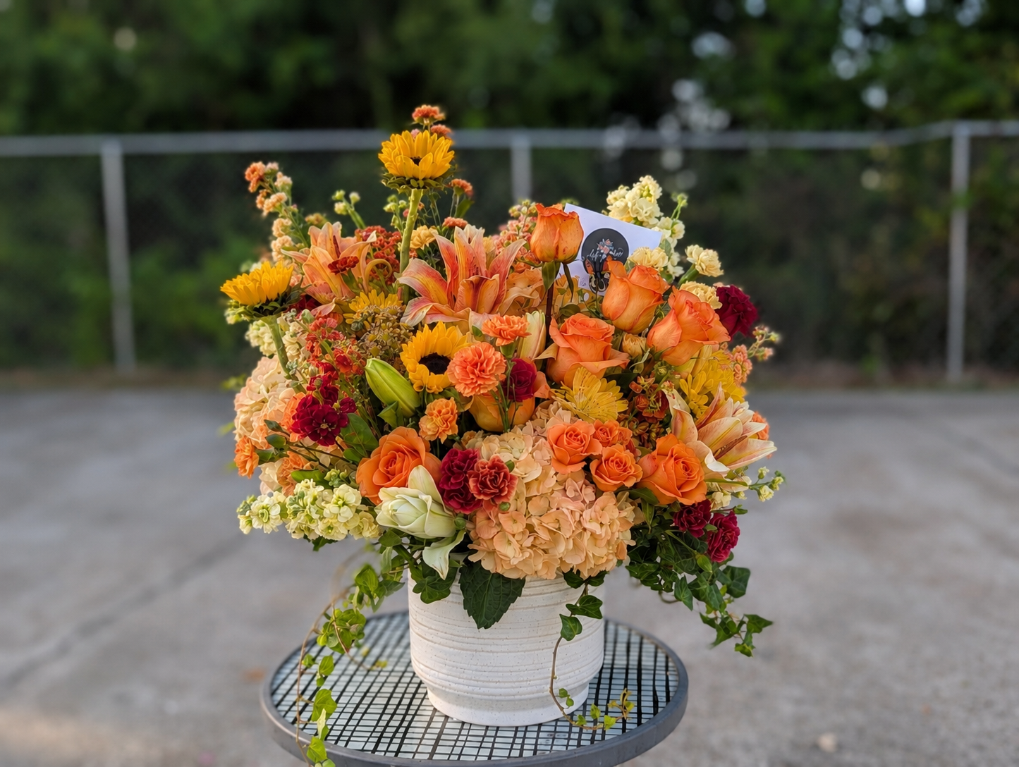 Autumn Celebration Vase filled with orange roses, yellow lilies, chrysanthemums, snapdragons, daisies, and seasonal fall flowers in a glass vase.