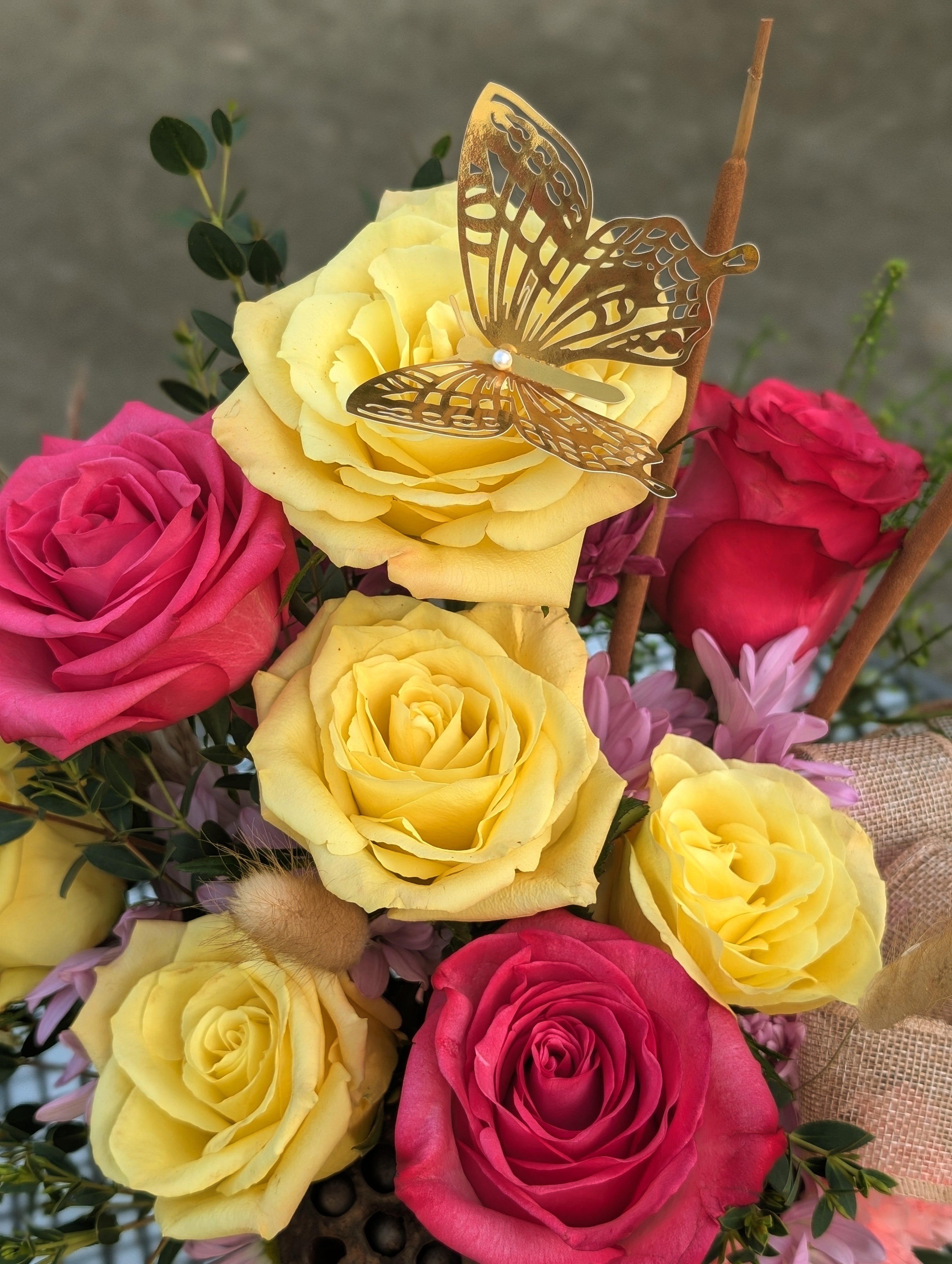 Yellow and pink roses accented with a decorative gold butterfly in the Butterfly Garden Keepsake arrangement.