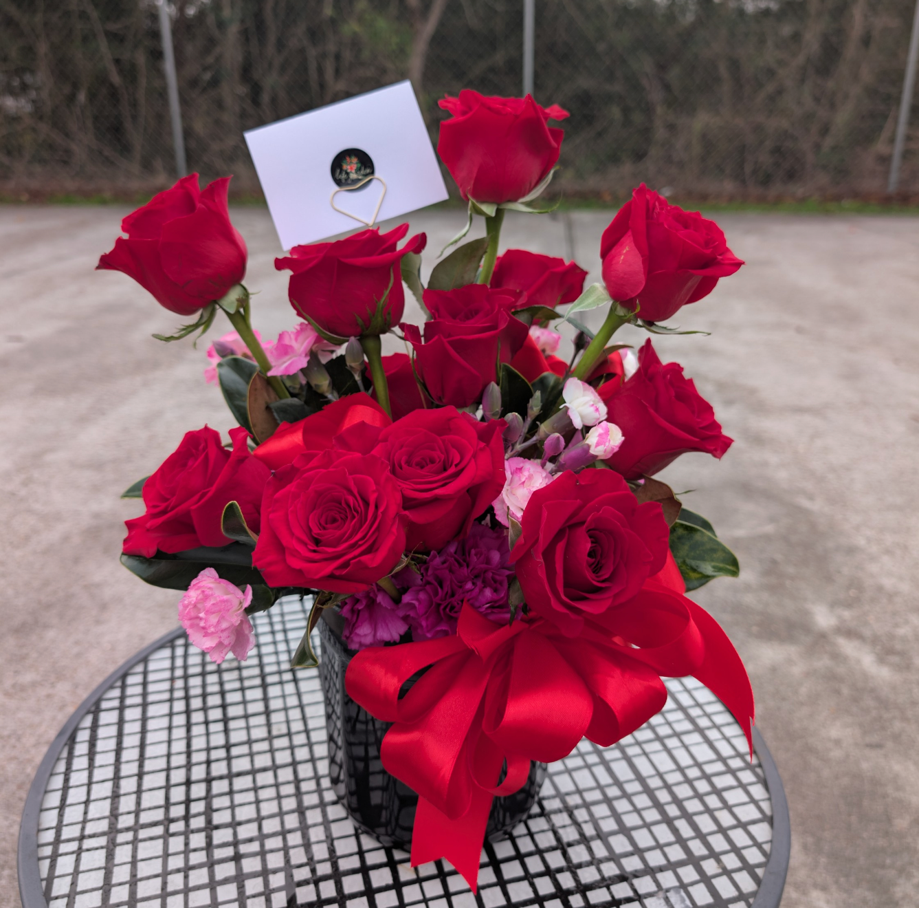 Red rose flower arrangement with pink and purple accents in ceramic vase
