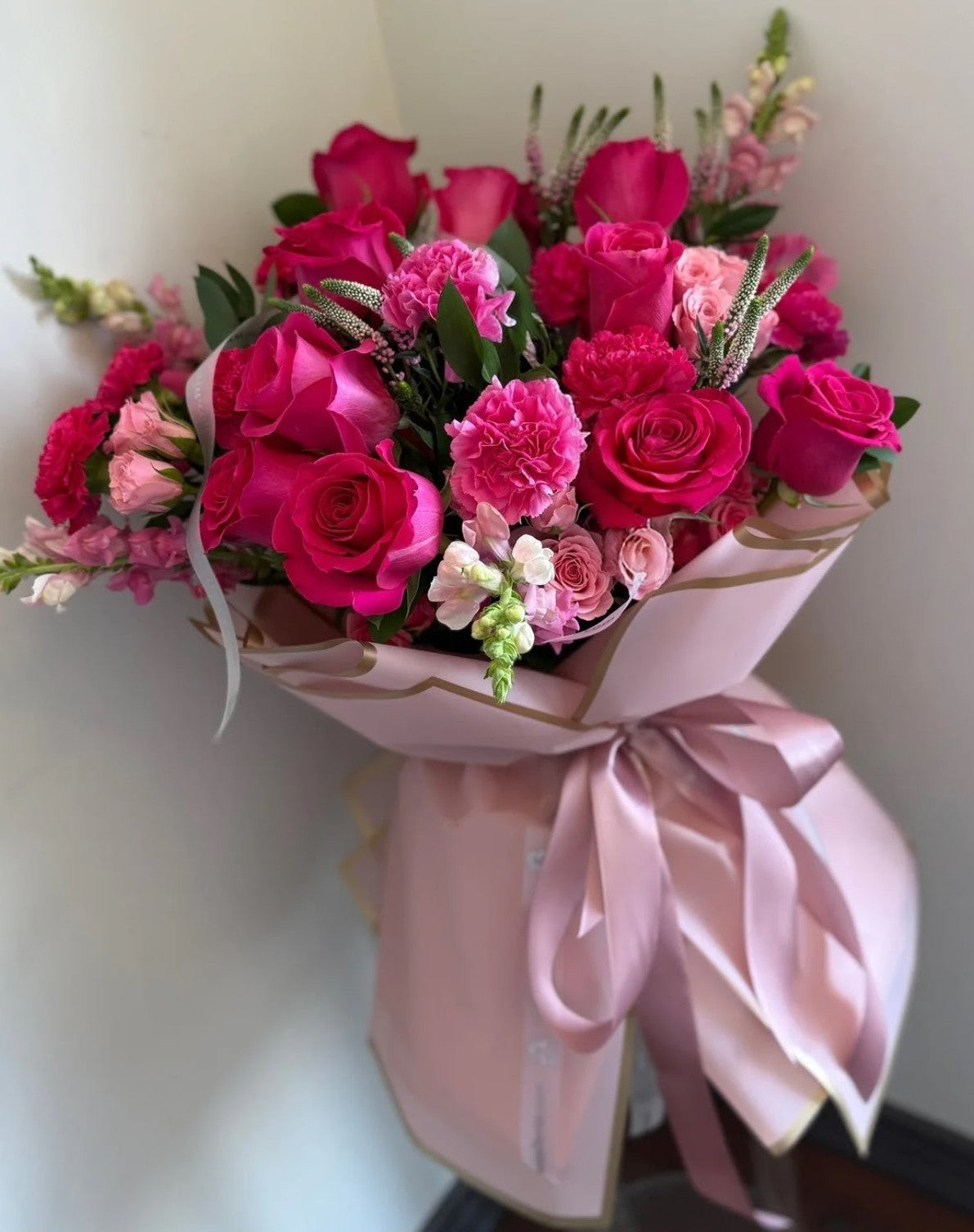 All-pink bouquet with pink roses, spray roses, and carnations wrapped in blush paper with satin ribbon.