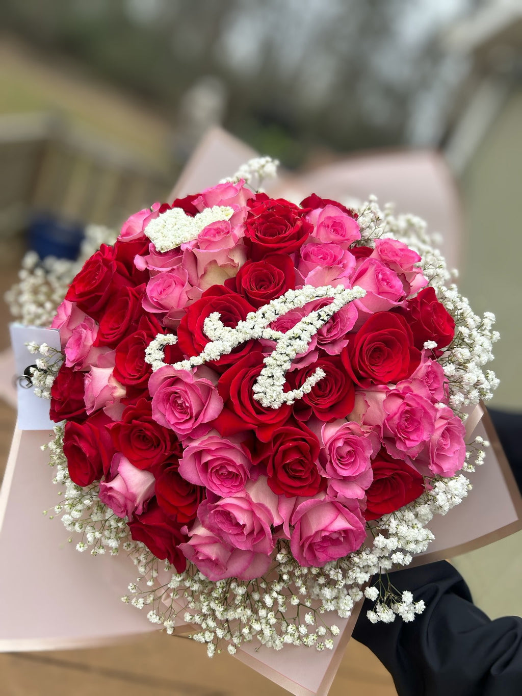 Pink and red rose bouquet wrapped in blush paper with baby’s breath monogram initial on top and baby’s breath accent around the bouquet.
