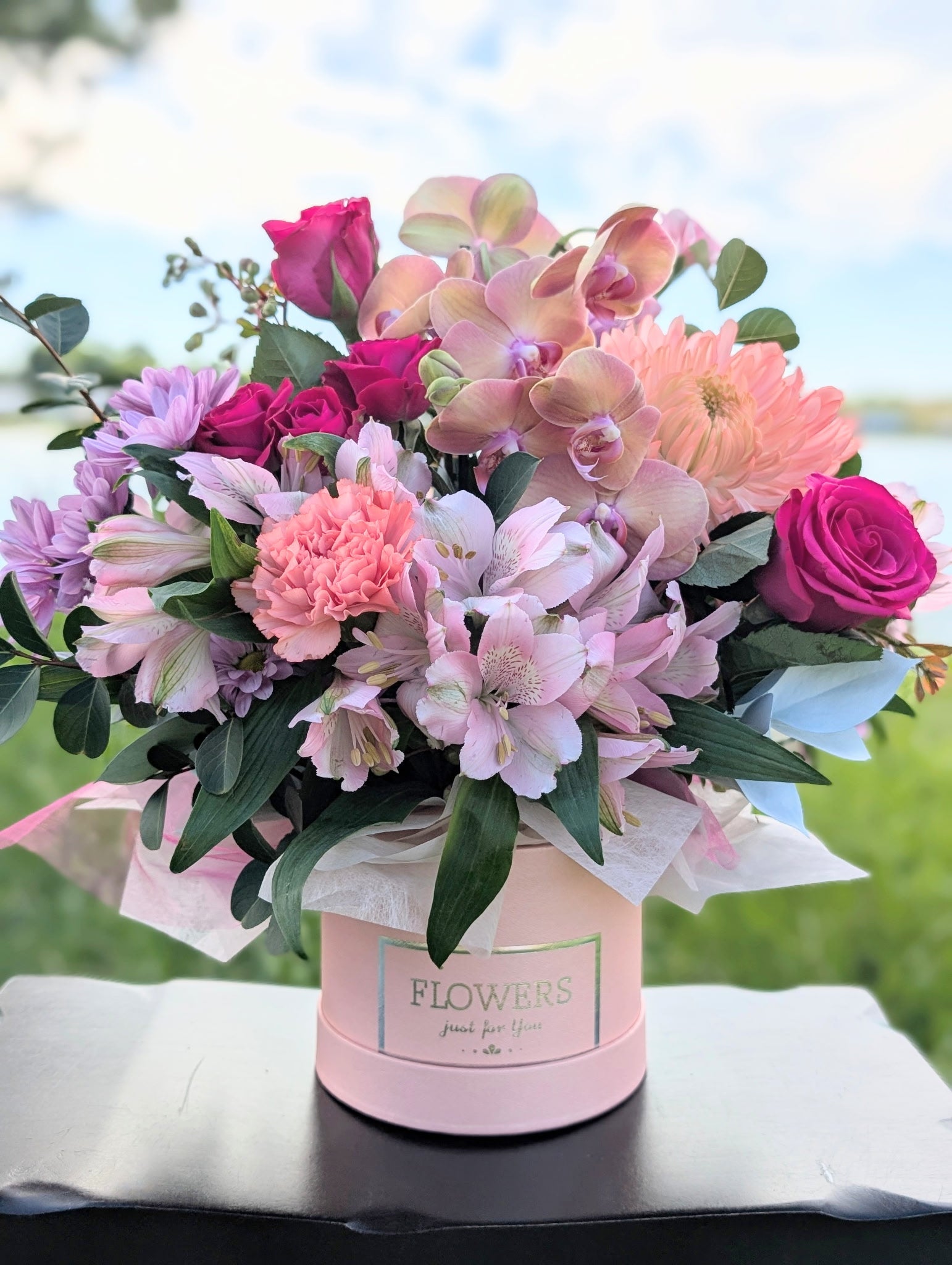 Pink Sunset floral arrangement with pink roses, orchids, alstroemeria, and lush greenery in a pink hatbox container.